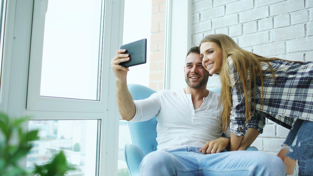 A couple sits together in their sunlit, modern living room, looking at a tablet and illustrating the financial freedom gained by saving thousands on real estate commissions.