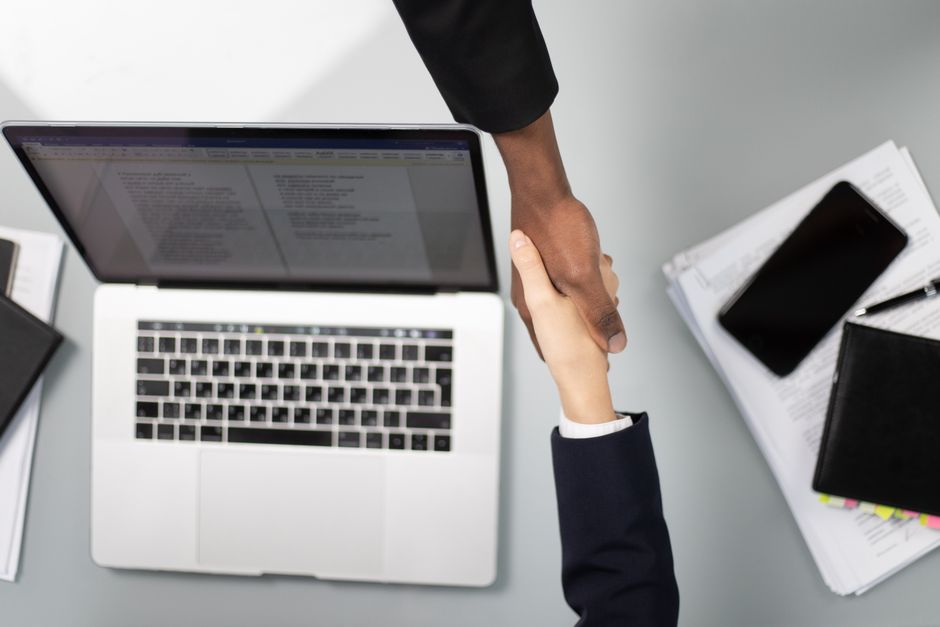 Professional real estate partner and a client, two people from diverse backgrounds, shake hands warmly on a sunny neighbor...